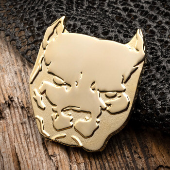 Polished gold bulldog head lapel pin with recessed detailing on a wooden surface.
