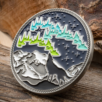Round challenge coin featuring a wolf howling at the northern lights over snowy mountains with a rope-textured border.