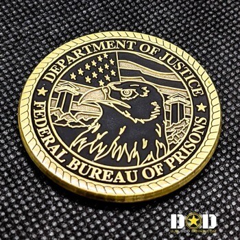 Gold and black challenge coin featuring the Federal Bureau of Prisons seal with an eagle head, American flag, and guard towers.