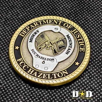 Gold and silver challenge coin for Department of Justice FCC Hazelton Misery Mountain featuring a rifle, handcuffs, and American flag.