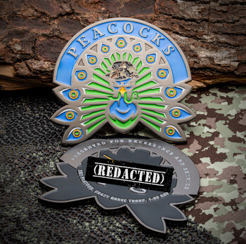 A custom challenge coin shaped like a peacock with blue and green enamel feathers, featuring the word Peacocks on a blue banner.