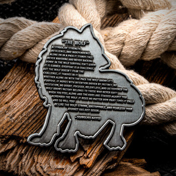Wolf-shaped silver challenge coin engraved with inspiring text resting on driftwood and nautical rope.