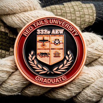 Red Tails University 332d AEW Graduate military challenge coin with copper finish resting on camouflage fabric and rope.