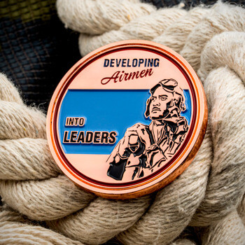Copper and blue military challenge coin reading Developing Airmen Into Leaders with a pilot portrait.