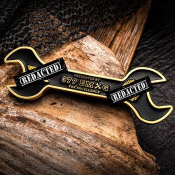 Custom wrench-shaped challenge coin featuring black enamel, gold plating, and the text Presented by 379 EMXG For Excellence.
