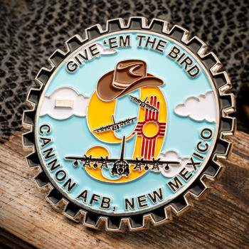 Gear-edged challenge coin for Cannon AFB, New Mexico featuring a large number 9, cowboy hat, aircraft silhouettes, and the Zia sun symbol on a light blue backgr
