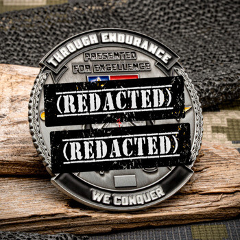 Antiqued silver challenge coin with the text Through Endurance We Conquer and Presented for Excellence on a wood and camouflage background.