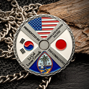 A circular challenge coin featuring the flags of the USA, South Korea, Japan, and Guam, presented by Lt Col Lucas Crouch.