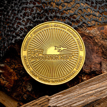 Gold challenge coin for DFW Innovation Next and Terminal F Concourse featuring a sunburst design and airplane silhouette.