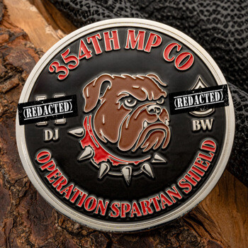 Round challenge coin featuring a bulldog with a spiked collar, text for 354th MP Co, and Operation Spartan Shield on a black and silver background.