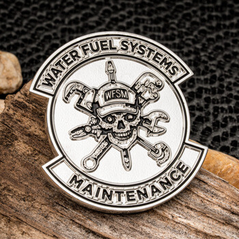 Silver challenge coin featuring a skull wearing a WFSM hat with crossed wrenches and tools, labeled Water Fuel Systems Maintenance.