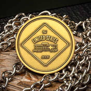 Gold challenge coin featuring a Limited Series train car emblem inside a diamond border, resting on a silver chain and wood background.