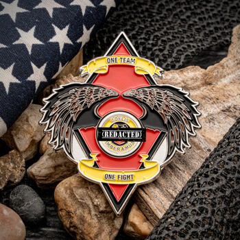 Diamond-shaped challenge coin with eagle wings, red and black enamel, and 'One Team One Fight' banners displayed with an American flag.
