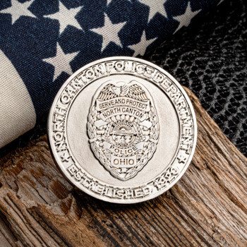 Silver North Canton Police Department challenge coin with badge emblem and American flag background.