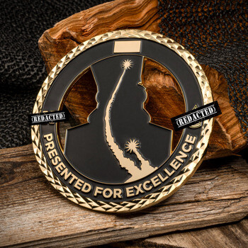 Gold challenge coin with black enamel, rocket launch silhouette, and diamond-cut edge displayed on wood.