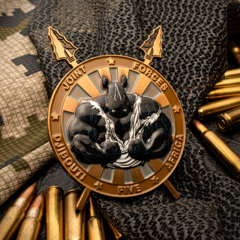 Joint Forces Africa Djibouti Five challenge coin featuring a muscular rhino and crossed spears, displayed with ammunition and camouflage gear.
