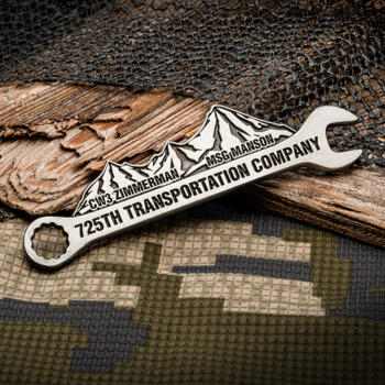 Wrench-shaped challenge coin featuring the 725th Transportation Company name, mountain range design, and names CW3 Zimmerman and MSG Manson.