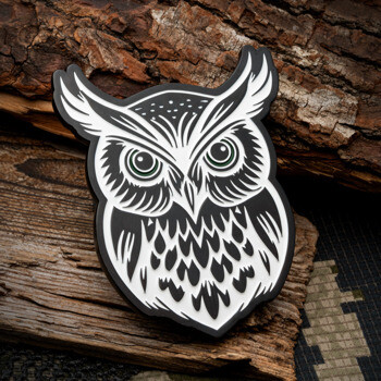 Black and white stylized owl lapel pin with intricate feather details on a wood background.