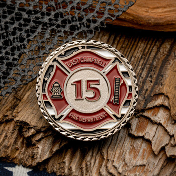 East Campbell Fire Department number 15 challenge coin with red Maltese cross, hydrant, and ladder icons on a wood and flag background.
