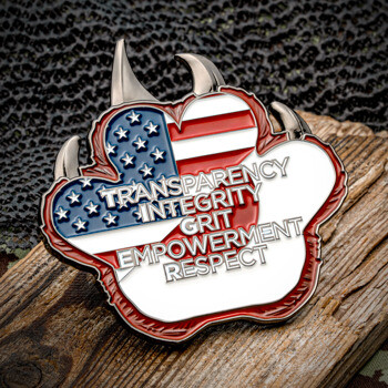 Paw-shaped challenge coin featuring the American flag design and the words transparency, integrity, grit, empowerment, and respect.