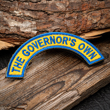 Embroidered arc-shaped patch with blue text reading The Governor's Own on a yellow background with a blue border.