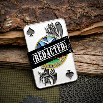 Ace of spades playing card challenge coin featuring aircraft maintenance graphics and a bat emblem against a wood and camouflage background.