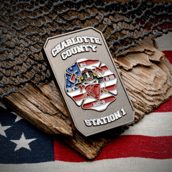 Rectangular antiqued silver challenge coin featuring a firefighter emblem with an American flag background, resting on wood over a US flag.