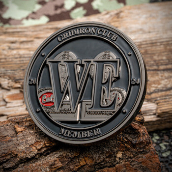 Black and silver Gridiron Club Member 2024 challenge coin featuring large WE initials and football imagery on a wooden background.