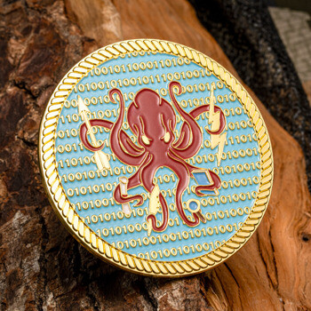 Gold-rimmed challenge coin featuring a red octopus with various tools on a blue background with binary code and a rope border.