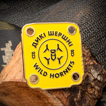 Square yellow enamel challenge coin with Wild Hornets logo and Ukrainian text, featuring four corner holes on a wood and camouflage background.