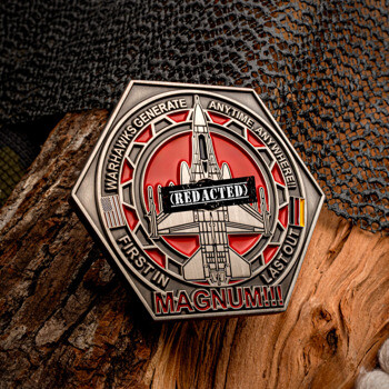 Hexagonal challenge coin featuring a fighter jet, red enamel background, and Magnum text resting on a wood log with netting.