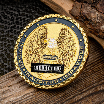 Gold challenge coin with a spread-wing eagle, black enamel border with Latin text, and diamond-cut edge displayed on wood.
