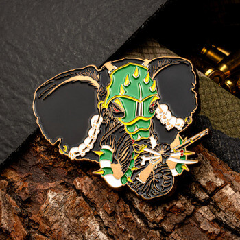 Custom lapel pin featuring a black elephant wearing green armor and skull tusks, resting on tree bark near bullet casings.