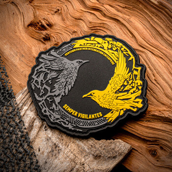 PVC patch featuring a grey and yellow raven design for CENTCOM Partner Integration Enterprise on a wood background.
