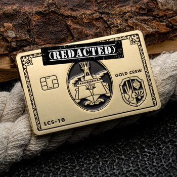 Rectangular gold challenge coin styled like a credit card with LCS-10 Gold Crew text and naval imagery on a rope background.