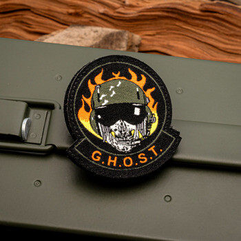 Embroidered G.H.O.S.T. patch featuring a skull in a flight helmet with orange flames, displayed on an olive drab ammo can.