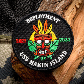 Circular embroidered patch featuring a colorful tiki mask with feathers and green leaves, labeled USS Makin Island Deployment 2023-2024.