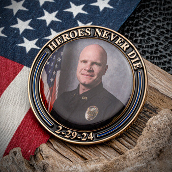 Challenge coin featuring a portrait of a police officer, the text Heroes Never Die, and a date, set against an American flag background.