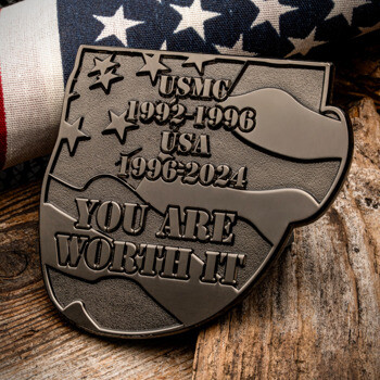 Antiqued silver shield challenge coin with USMC and USA service dates and the phrase You Are Worth It over an American flag background.