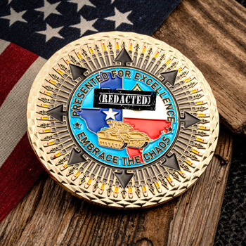 Gold-plated challenge coin featuring the Texas state flag, a military tank, and a compass rose with bullet patterns on a wooden surface next to a US flag.