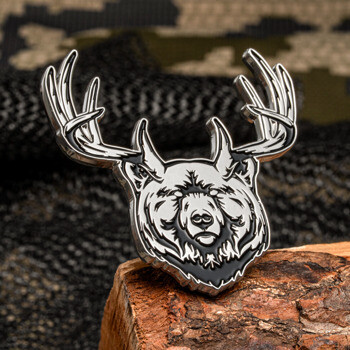 Silver and black enamel lapel pin featuring a bear head with deer antlers resting on a piece of wood.