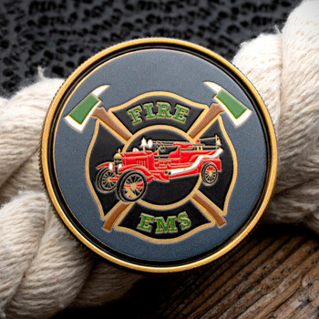 Circular challenge coin featuring a Maltese cross, fire axes, vintage red fire engine, and the words Fire EMS, displayed on a textured rope background.