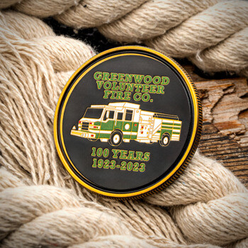 Greenwood Volunteer Fire Co. centennial challenge coin featuring a green and white fire engine on a black background, framed by a thick hemp rope.