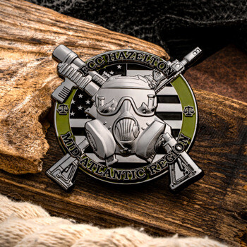 FCC Hazelton Mid-Atlantic Region challenge coin featuring a gas mask, crossed rifles, and a black-and-white American flag on a wooden background.