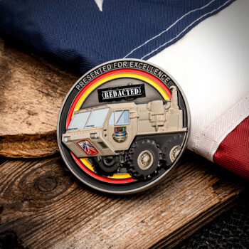 Custom challenge coin featuring a military transport vehicle on a red, yellow, and black background, displayed next to an American flag.
