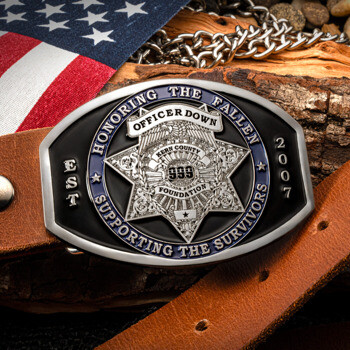 Custom silver and black belt buckle featuring the Kern County 999 Foundation star emblem, set on a brown leather belt with an American flag background.