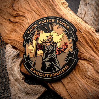 Custom PVC patch for Task Force Yuma Executioners depicting a spiked warrior figure holding a staff against a yellow and orange sunburst, displayed on wood.