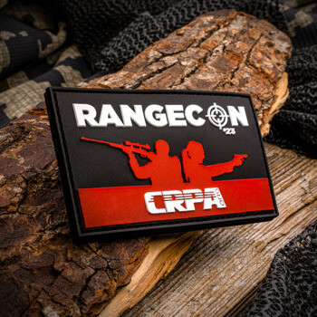 Rectangular PVC patch for RangeCon '23 featuring a red silhouette of two shooters on a black background with CRPA logo, displayed on a piece of wood.