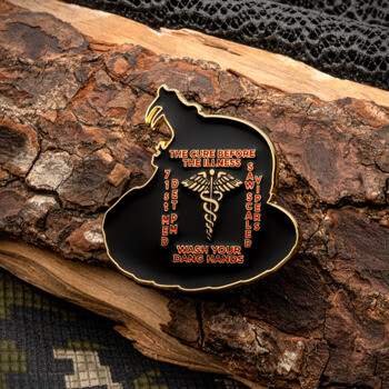 A custom-shaped black enamel lapel pin depicting a coiled snake shape with a caduceus symbol, orange text reading 'The Cure Before the Illness', and gold platin