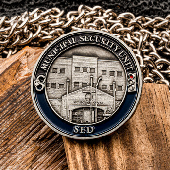 Municipal Security Unit SED challenge coin featuring a detailed 3D engraving of a municipal court building, displayed on wood with a silver chain.